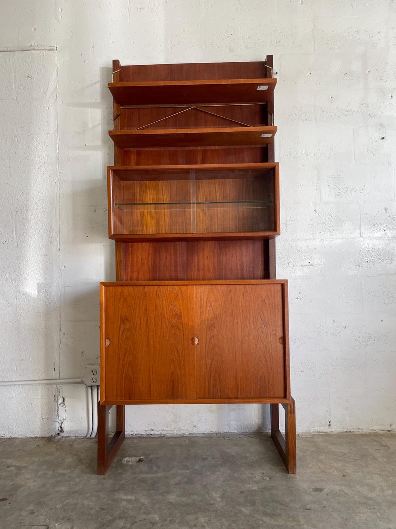 Op de afbeelding: Een teak houten kast in mid-century modern stijl met een glazen vitrine en twee deuren. De kast heeft een warme bruine kleur en een eenvoudig, elegant ontwerp.