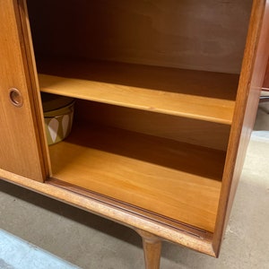 May include: A wooden cabinet with a single door and two shelves. The door is closed and the shelves are empty. The cabinet is made of light wood and has a simple design.