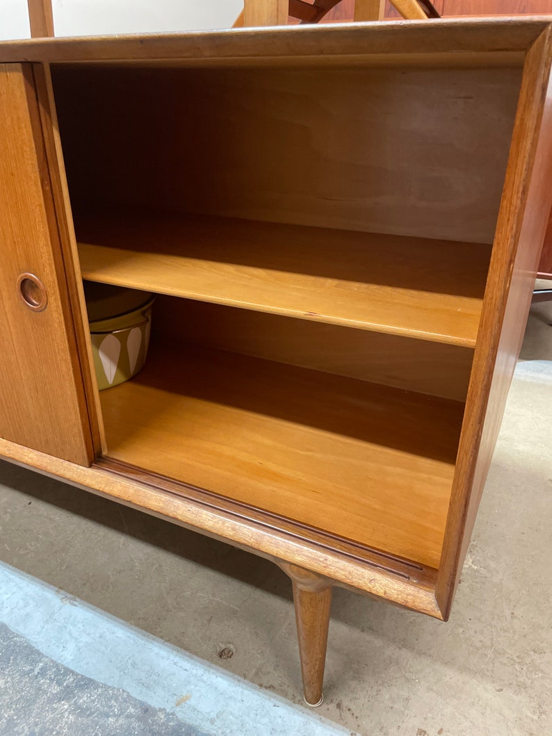 May include: A wooden cabinet with a single door and two shelves. The door is closed and the shelves are empty. The cabinet is made of light wood and has a simple design.