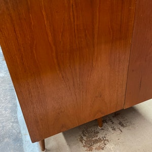 May include: A close-up of a wooden cabinet with a light brown finish. The cabinet has a simple design with a smooth surface and visible wood grain. The cabinet is sitting on a light gray floor.