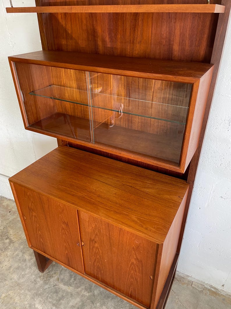 Op de afbeelding: Een hoge houten kast met glazen deuren en planken. De kast heeft een lager gedeelte met twee massieve deuren. De kast is gemaakt van een rijk, roodbruin hout.