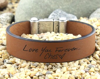 May include: Brown leather bracelet with a silver magnetic clasp. The bracelet is engraved with the text "Love You Forever... Ches"