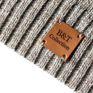 May include: A close-up of a brown leather patch with the text "B&T Collection" sewn onto a gray knitted fabric.