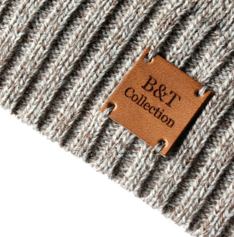 May include: A close-up of a brown leather patch with the text "B&T Collection" sewn onto a gray knitted fabric.