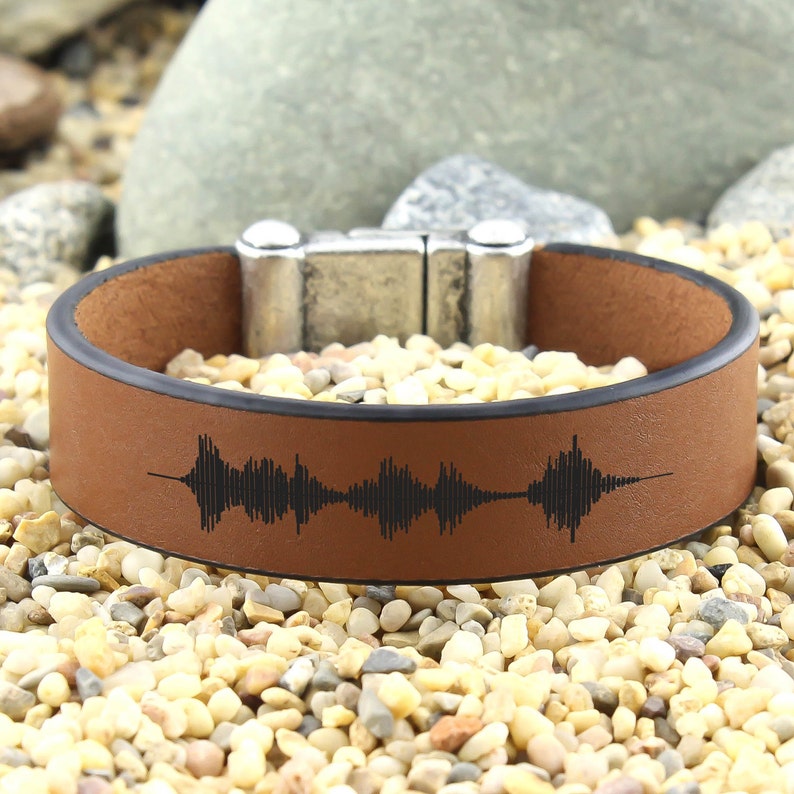 May include: A brown leather bracelet with a black sound wave design and a silver magnetic clasp.