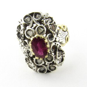 May include: A silver ring with a red gemstone set in a filigree design. The ring is accented with small diamonds.