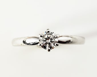 May include: A simple silver engagement ring with a single round diamond.