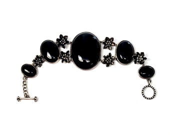 May include: A black onyx bracelet with silver floral accents. The bracelet has a clasp closure and is made of metal.
