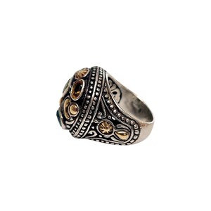 May include: A silver ring with a large, ornate setting featuring green and yellow gemstones and gold accents.
