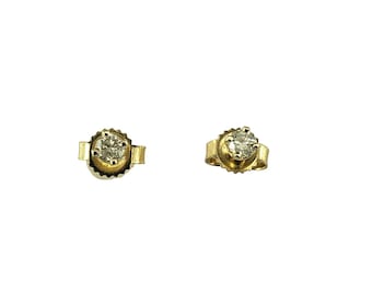 May include: A pair of gold stud earrings, each featuring a round, clear gemstone. The earrings have a classic design with a simple, elegant setting. The gemstones are the focal point, set in a gold bezel.