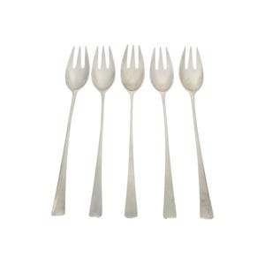 May include: Five silver serving forks with long, slender handles and three tines. The forks are arranged against a white background, with the tines facing up. The forks are made of a shiny, reflective metal.