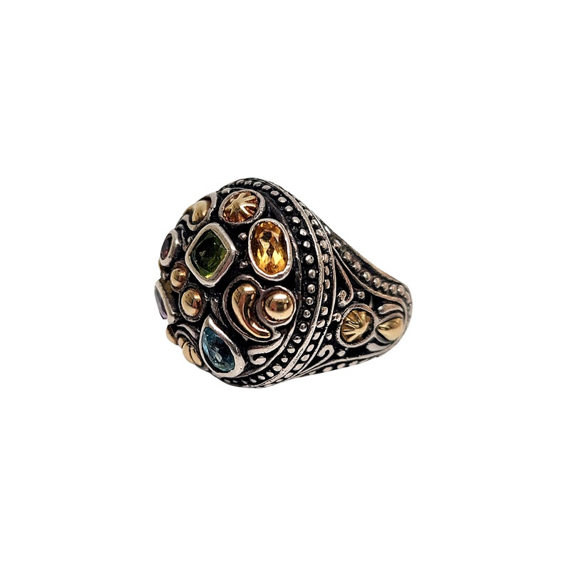 May include: A silver ring with a domed top set with colourful gemstones and gold accents. The ring has a detailed design with intricate patterns.