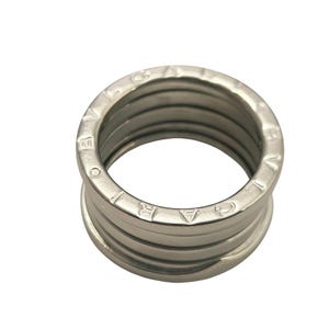 May include: A silver-colored ring with a ribbed design. The ring has a series of horizontal bands, with the brand name engraved around the top edge. The ring is a classic piece of jewelry.