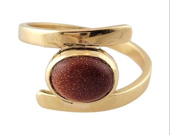 May include: A gold ring with a round, brown stone set in the center. The ring has a simple, modern design.