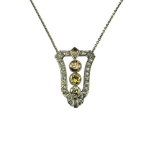 May include: A silver necklace with a pendant featuring three round yellow gemstones surrounded by smaller clear gemstones. The pendant is shaped like a teardrop and has a geometric design.