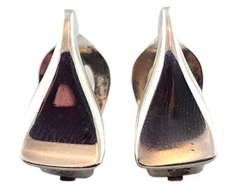 Puede incluir: Un par de pendientes de plata con forma triangular. Los pendientes tienen un acabado liso y pulido.