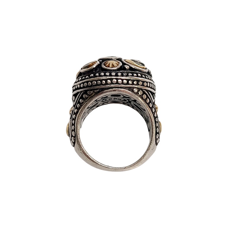 May include: A silver ring with a round, textured top. The top of the ring is decorated with small, gold-coloured accents.