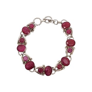 May include: A silver bracelet featuring oval and round ruby gemstones. The bracelet has a toggle clasp and is composed of multiple links, each holding a large ruby and two smaller rubies. The rubies are a deep red color.