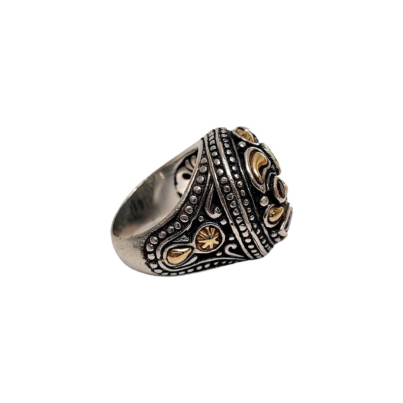 May include: A silver ring featuring a large, round, faceted gemstone set in a gold-toned bezel. The ring is adorned with intricate, detailed designs in silver and gold.