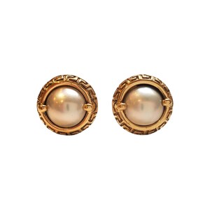 May include: A pair of gold tone earrings with a pearl center and a geometric design around the edge.