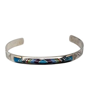 May include: A silver cuff bracelet with a colorful inlaid design. The inlay features blue, green, purple, and red geometric shapes. The bracelet has etched patterns on the ends.
