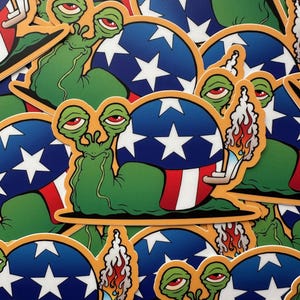 May include: A stack of stickers featuring a cartoon snail with a green body and red, white, and blue shell. The snail is holding a lit cigarette in its hand. The shell is decorated with a design resembling the American flag.