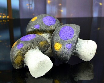 May include: Three decorative mushroom-shaped bath bombs with a black base and purple and gold polka dots.
