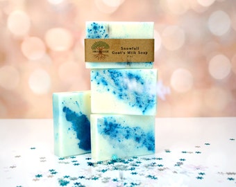 May include: Four bars of white goat's milk soap with blue swirls. The top bar has a brown label that reads "Snowfall Goat's Milk Soap 4 oz".