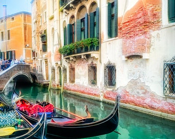 Può includere: Una vista pittoresca di un canale veneziano con gondole. Le gondole nere sono in primo piano, con un ponte e degli edifici sullo sfondo. L'acqua è di un verde vibrante e gli edifici hanno facciate invecchiate.