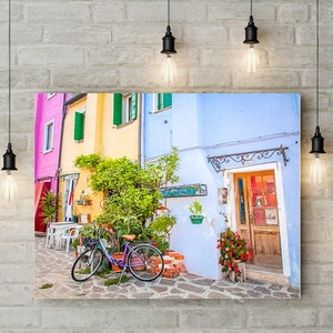 Pu&ograve; includere: Un edificio colorato in stile vintage con una porta blu e una bicicletta parcheggiata davanti. L'edificio ha una facciata rosa, gialla e blu con persiane verdi. La bicicletta &egrave; viola e ha un cestino sul manubrio.