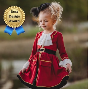 Puede incluir: Una niña pequeña con un disfraz de pirata rojo y negro con un cuello de volantes blanco, un cinturón negro y ribetes dorados. Lleva medias negras y botas negras de cordones. La niña está de pie en un campo de hierba.