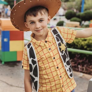 Puede incluir: Un ni&ntilde;o peque&ntilde;o vestido como Woody de Toy Story. Lleva una camisa de cuadros amarillos y rojos con un sombrero de vaquero marr&oacute;n y un chaleco negro y blanco con una estrella de sheriff.