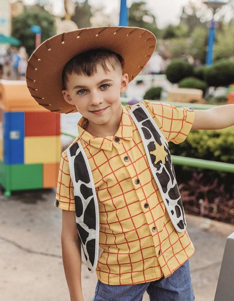 Puede incluir: Un ni&ntilde;o peque&ntilde;o vestido como Woody de Toy Story. Lleva una camisa de cuadros amarillos y rojos con un sombrero de vaquero marr&oacute;n y un chaleco negro y blanco con una estrella de sheriff.