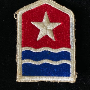 May include: A white, red, and blue embroidered patch with a white star and three white waves on a blue background. The patch is surrounded by a white border.