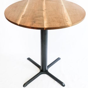 May include: A round wooden table top with a black metal base. The table top is made of wood with a natural finish. The base is a simple cross shape with four legs.