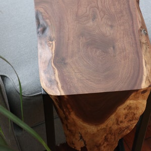 May include: A wooden side table with a live edge top and black metal legs. The wood has a rich brown color and a natural grain pattern.