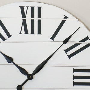 May include: White farmhouse style clock with black Roman numeral hour markers and black hands. The clock face is made of wood planks.
