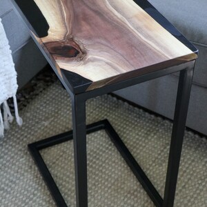 May include: A black metal side table with a wooden top and black epoxy resin inlay. The table has a simple, modern design and is perfect for a living room or bedroom.