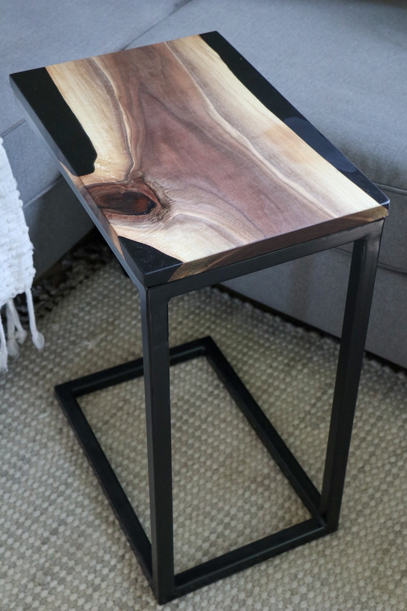 May include: A black metal side table with a wooden top and black epoxy resin inlay. The table has a simple, modern design and is perfect for a living room or bedroom.