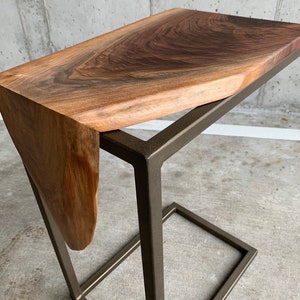 May include: A wooden side table with a live edge walnut top and a black metal frame. The table has a unique, organic shape.
