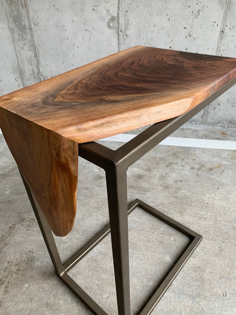 May include: A wooden side table with a live edge walnut top and a black metal frame. The table has a unique, organic shape.