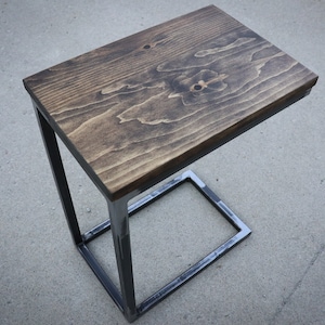 May include: A dark brown wooden tabletop with a black metal frame. The table is a side table or end table with a rectangular top and a square base.
