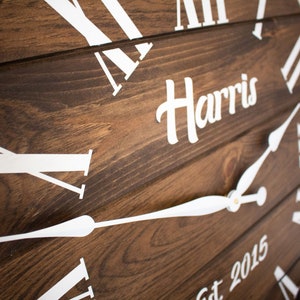 Puede incluir: Un reloj de madera marr&oacute;n con marcas de n&uacute;meros romanos blancos y manecillas blancas. La esfera del reloj tambi&eacute;n incluye el texto "Harris Est 2015".