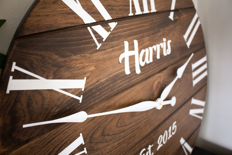 Puede incluir: Un reloj de madera marr&oacute;n con marcas de n&uacute;meros romanos blancos y manecillas blancas. La esfera del reloj tambi&eacute;n incluye el texto "Harris Est 2015".