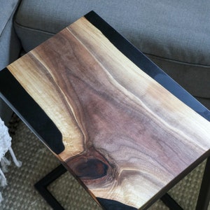 May include: A wooden side table with a black epoxy resin inlay. The table has a natural wood finish and a black metal frame.