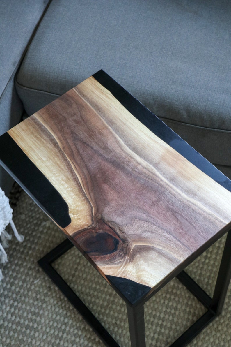 May include: A wooden side table with a black epoxy resin inlay. The table has a natural wood finish and a black metal frame.