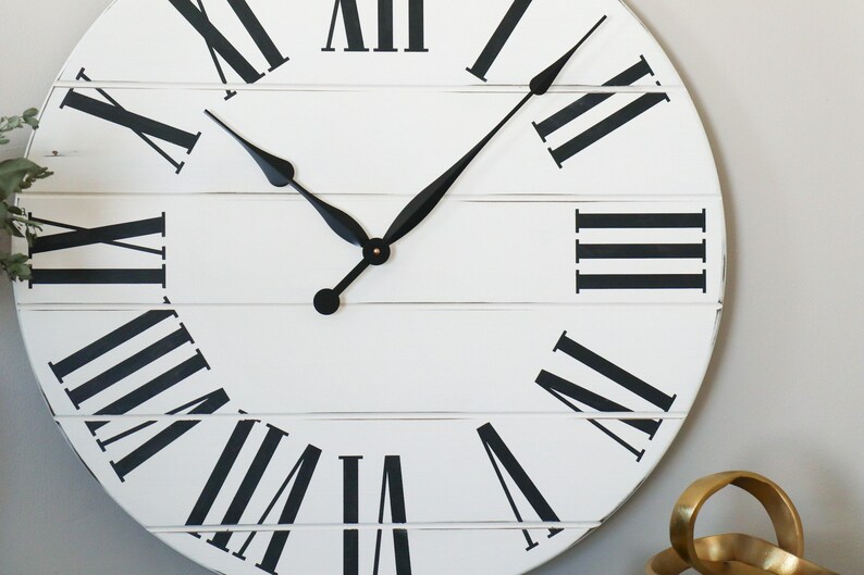 May include: A large, white, round clock with black Roman numeral markings and black hands. The clock face is made of wood planks.
