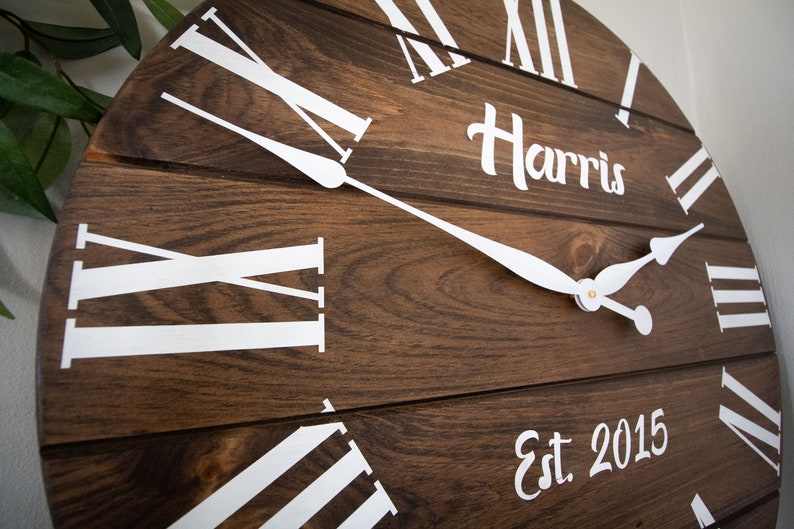 Puede incluir: Un reloj de madera marr&oacute;n con n&uacute;meros romanos blancos y agujas blancas. La esfera del reloj tambi&eacute;n tiene el texto "Harris Est 2015".
