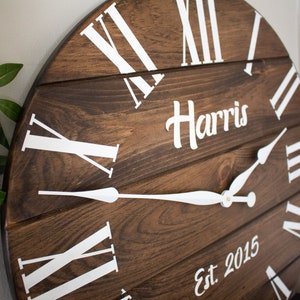 Puede incluir: Un reloj de madera marr&oacute;n con marcas de n&uacute;meros romanos blancos y manecillas blancas. La esfera del reloj tambi&eacute;n incluye el texto "Harris Est 2015".