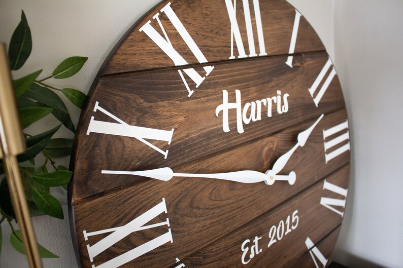 Puede incluir: Un reloj de madera marr&oacute;n con marcas de n&uacute;meros romanos blancos y manecillas blancas. La esfera del reloj tambi&eacute;n incluye el texto "Harris Est 2015".